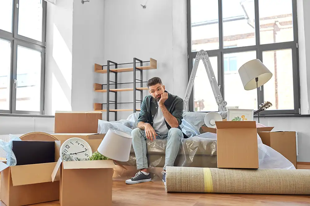 Umzug, Zwangsräumung und Immobilienkonzept – trauriger Mann mit Kartons in seiner neuen Wohnung