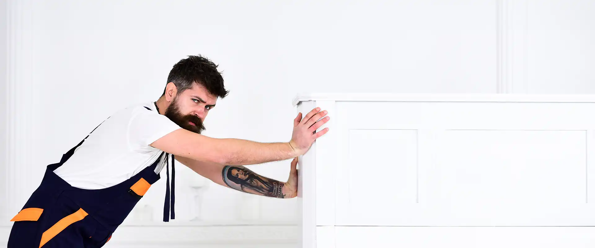 Mann mit Bart und Schnurrbart, Arbeiter in Overalls schiebt Klavier, weißer Hintergrund. Kurier liefert Möbel bei Umzug, Umzug.